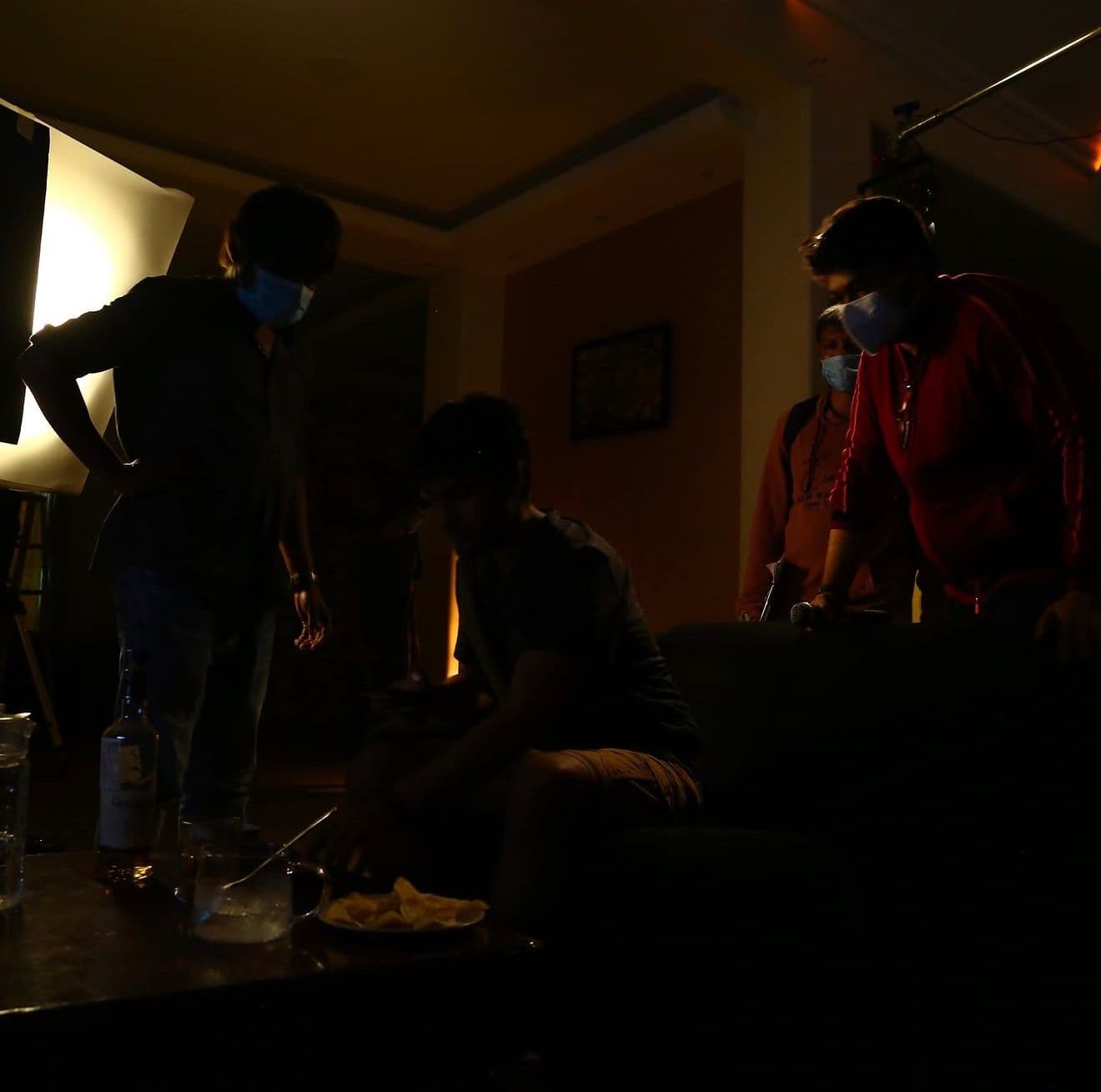 A group in face masks gathered around a low table with drinks and snacks in a dimly lit room