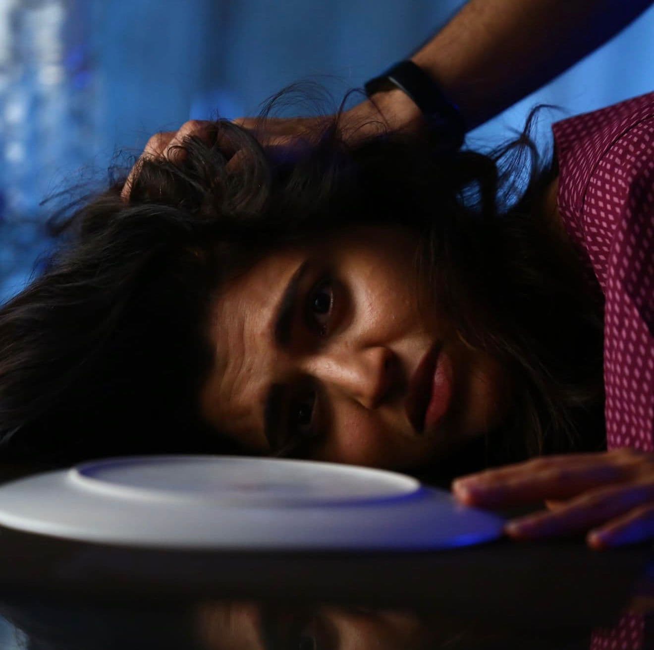 Close-up of an actress with her head tilted back on a table, dramatic blue-lit shot