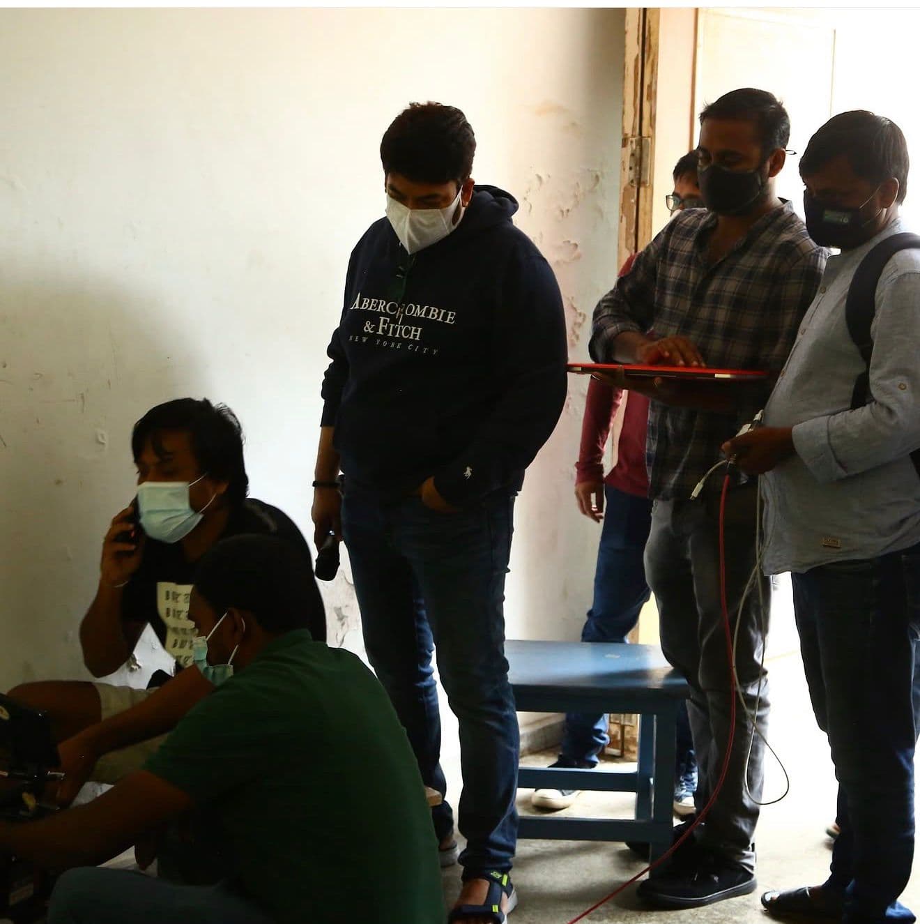 Crew members in face masks gathered in a doorway with camera equipment, one on a phone call