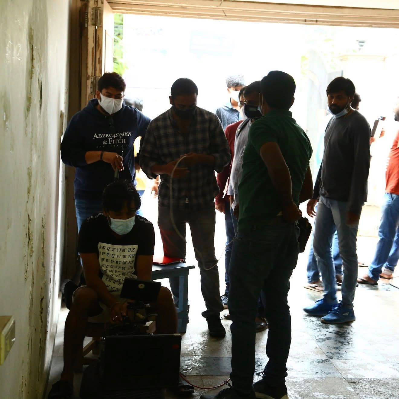 A larger crew group loading camera equipment at a garage-style entrance in daylight