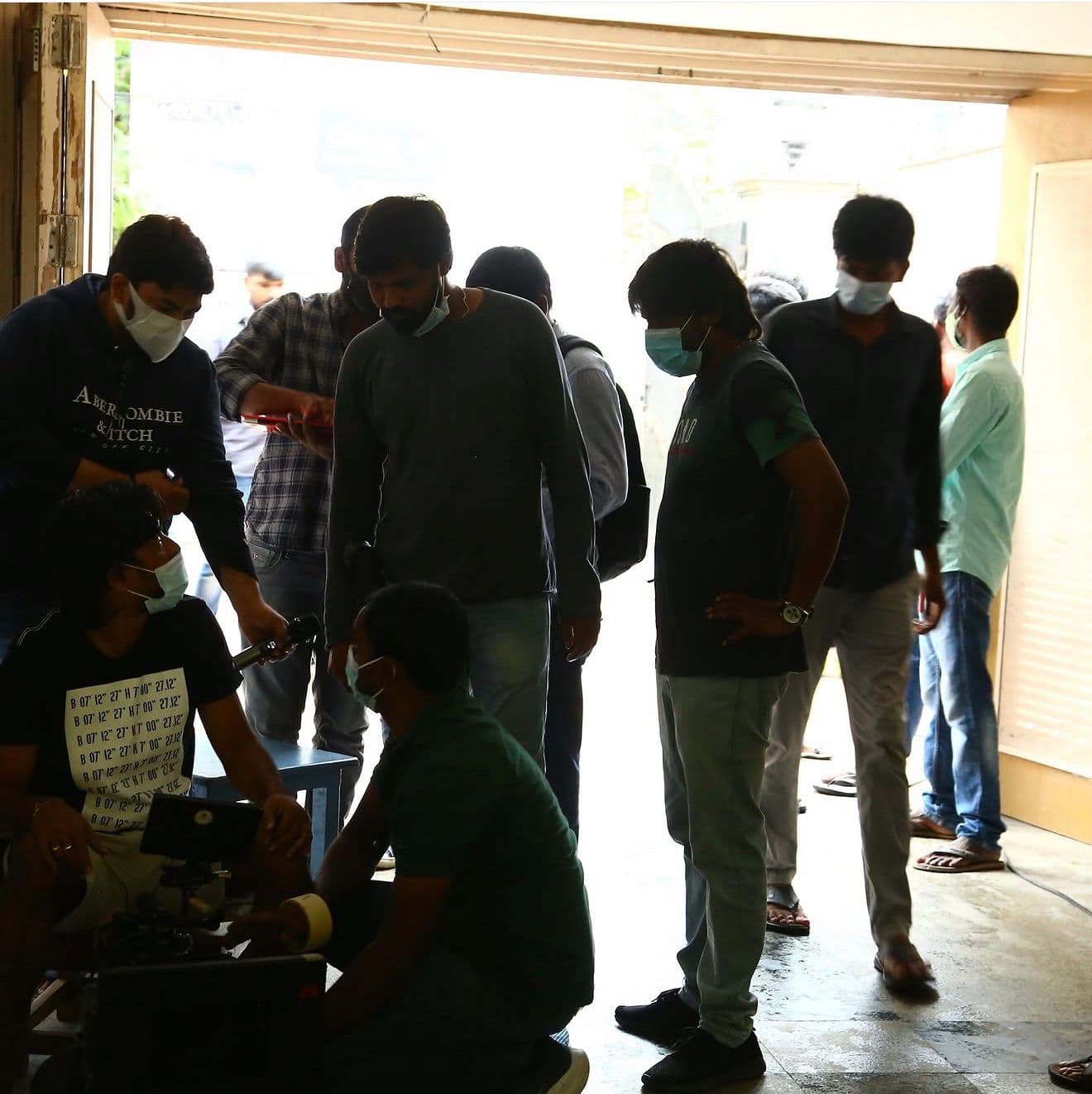 A bigger crew gathered at a garage-style entrance, camera equipment set up in natural daylight