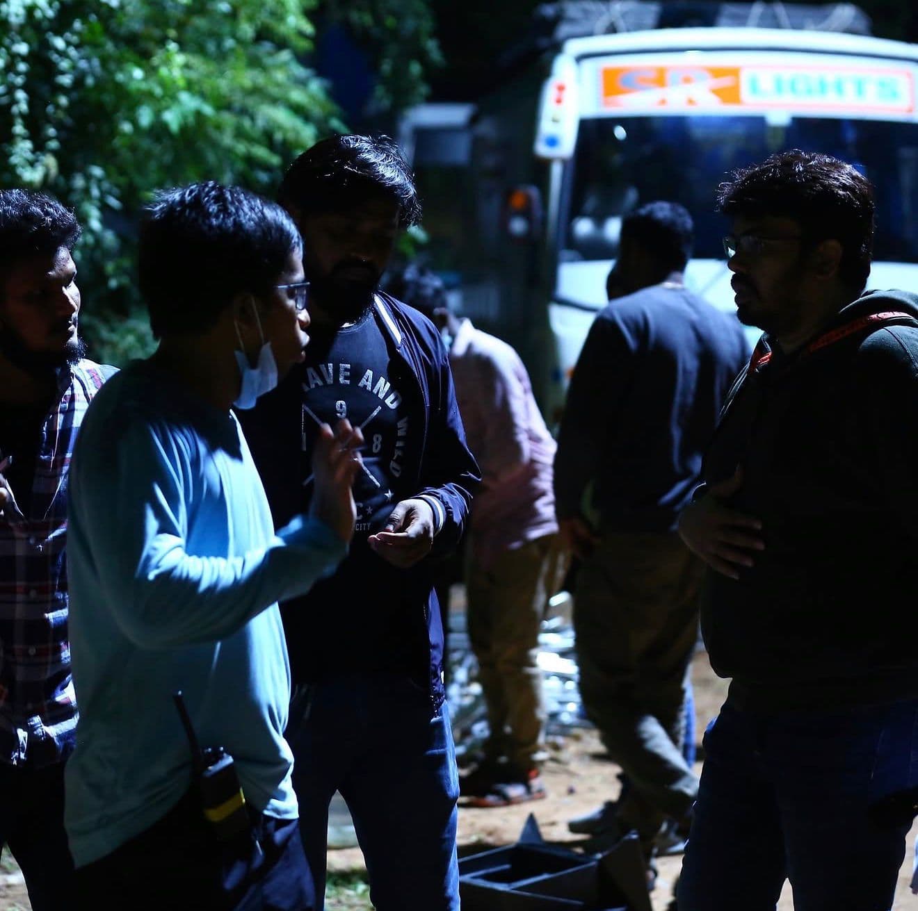 Crew members talking on a footpath at night beside a production lighting truck