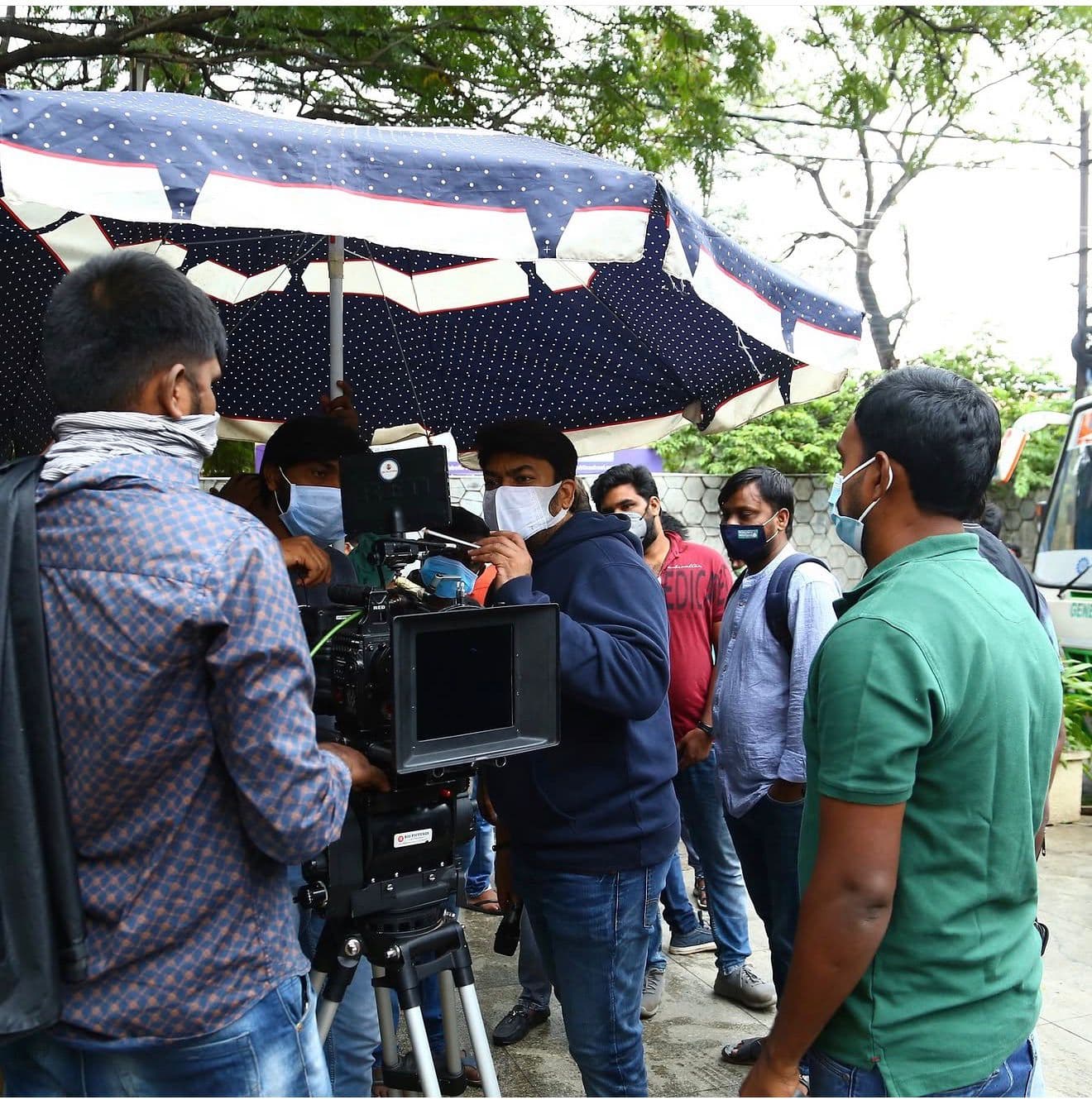 A crew member operating a camera rig under an umbrella outdoors in daylight