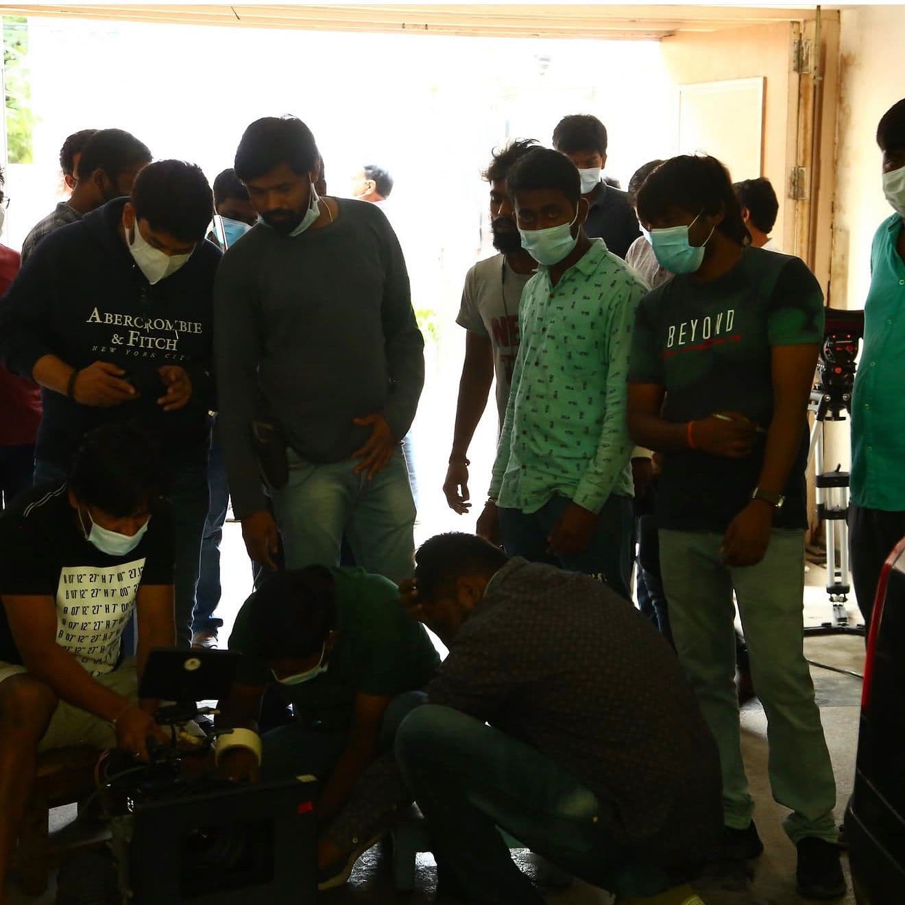 A larger crew group gathered at a garage-style entrance around camera equipment in daylight