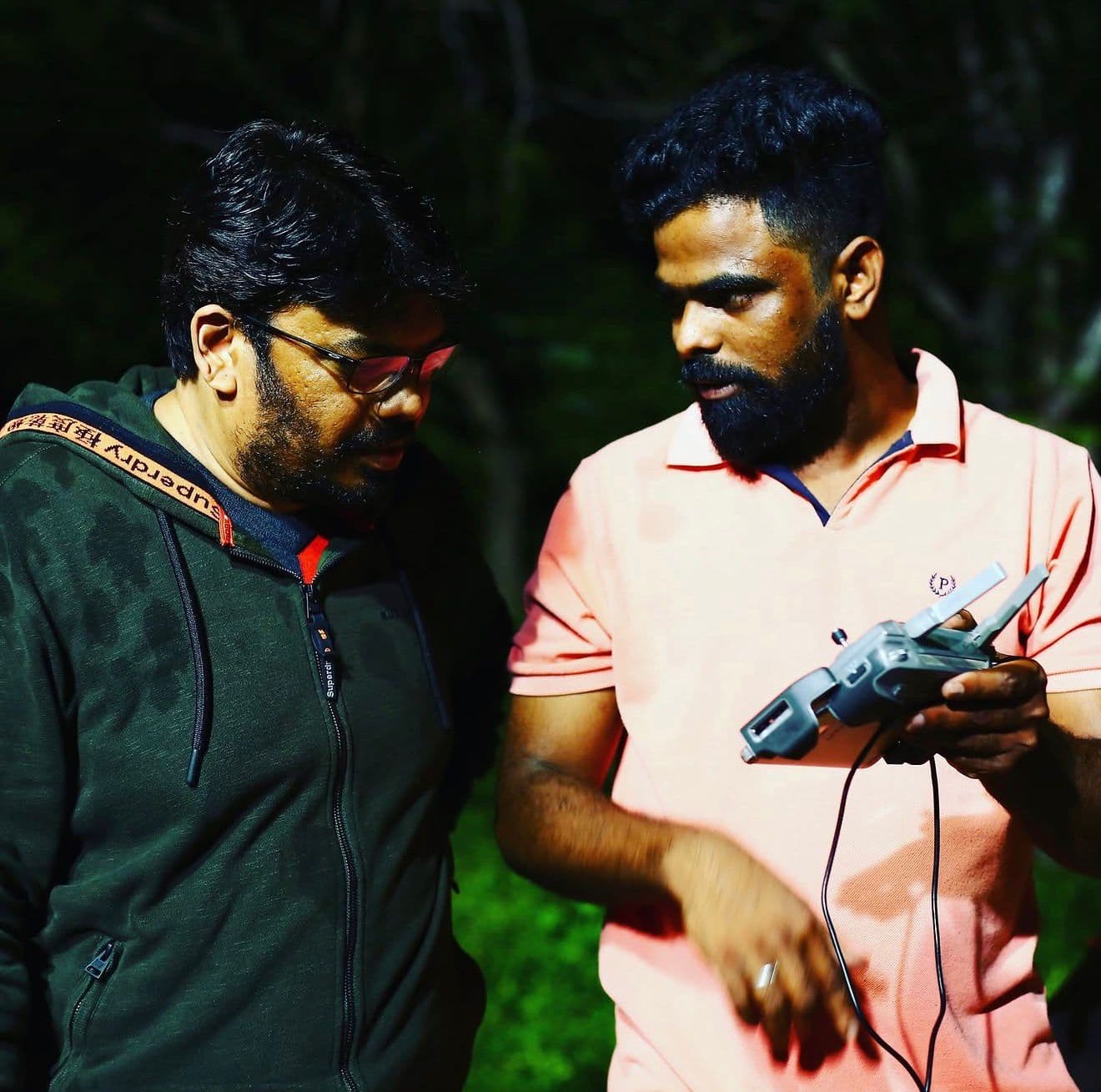 Two crew members examining a handheld transmitter device together at night outdoors