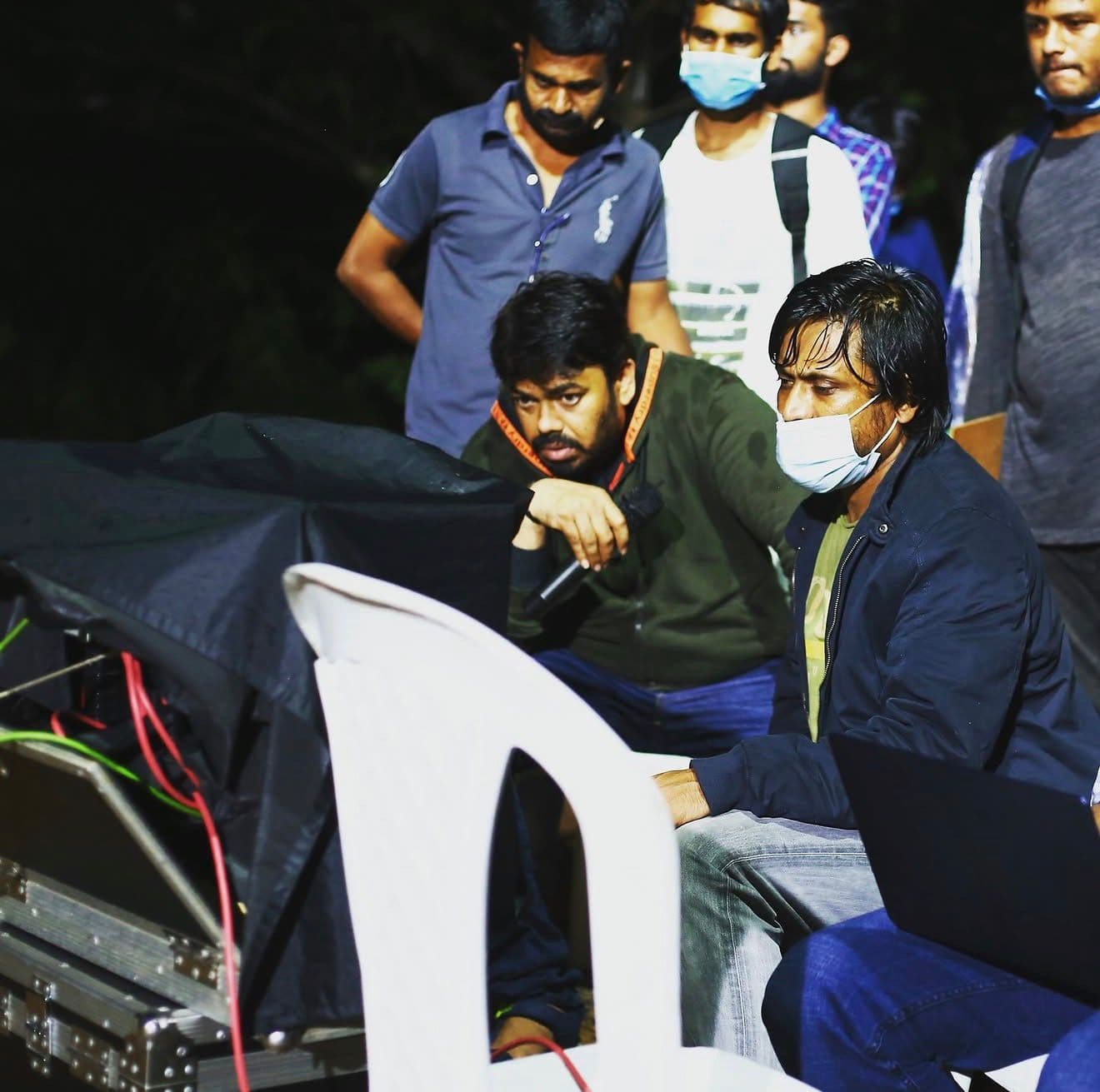 Two crew members reviewing a monitor rig at night, others standing behind them
