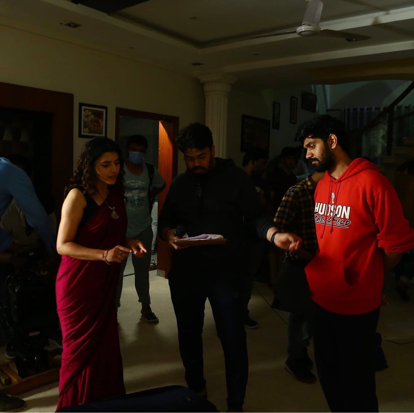 An actress in a saree consulting notes with two crew members in a house interior