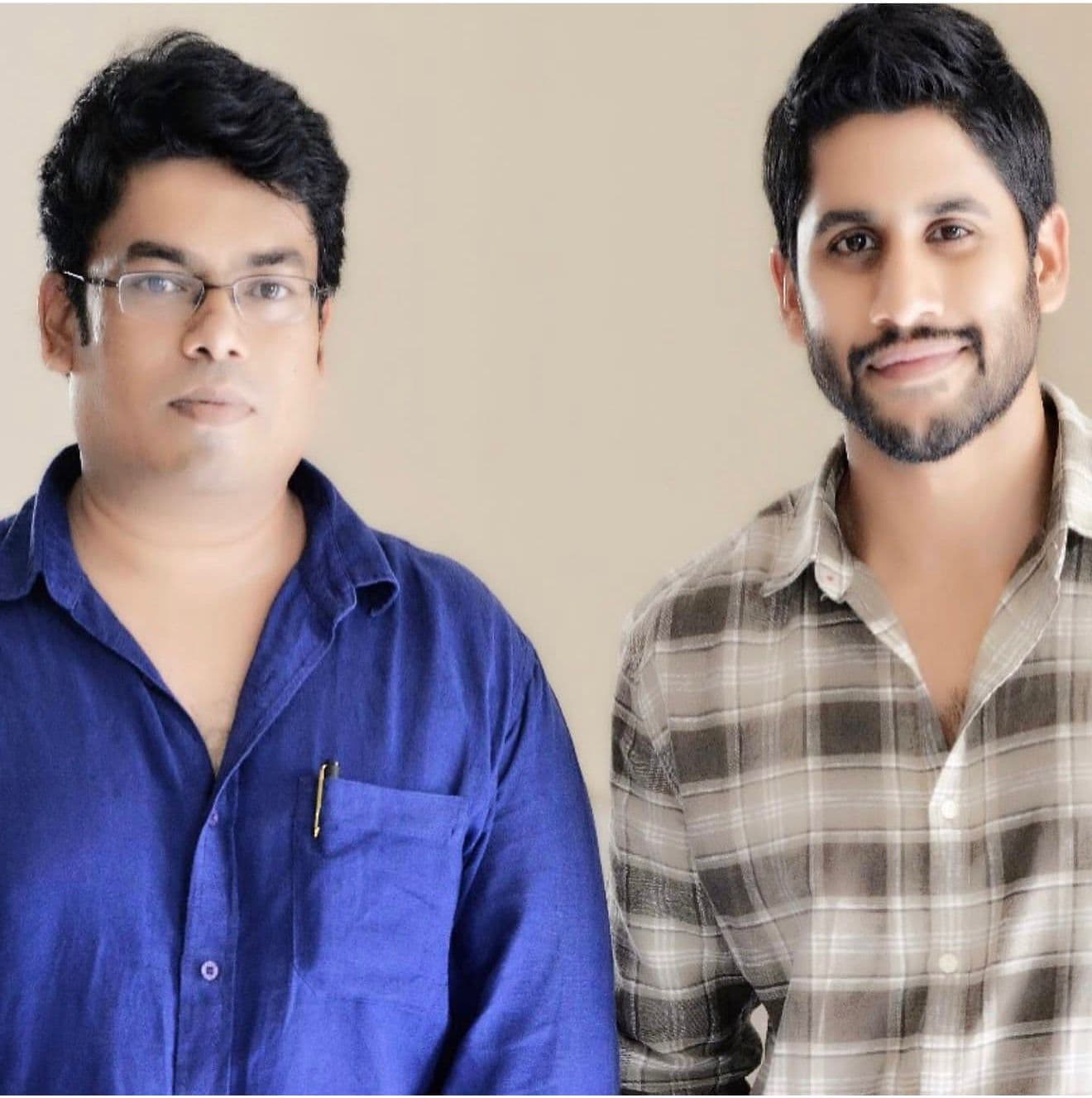 Two men posing for a portrait against a plain studio backdrop, one wearing glasses