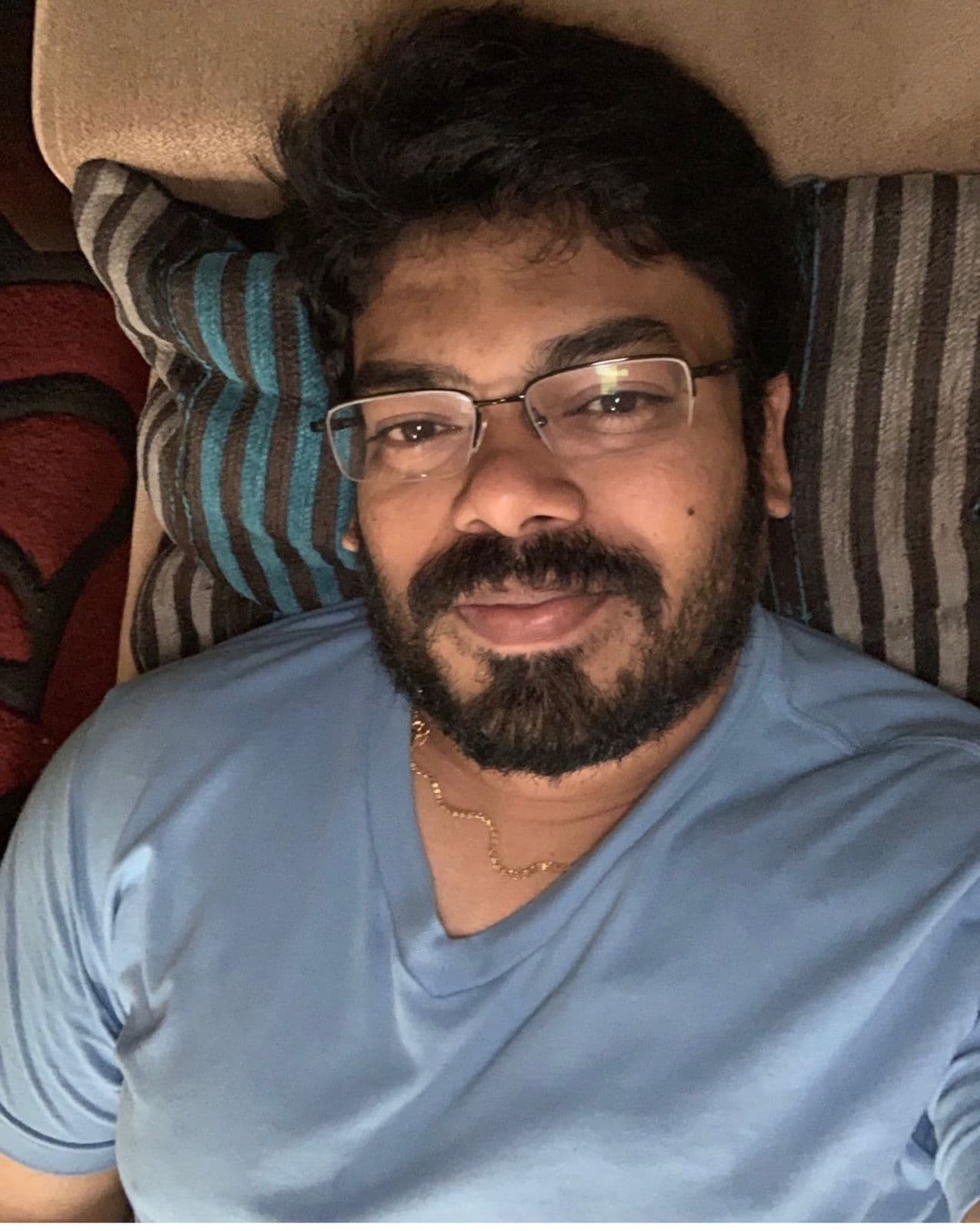 A close, selfie-style portrait of a man reclining on a striped sofa
