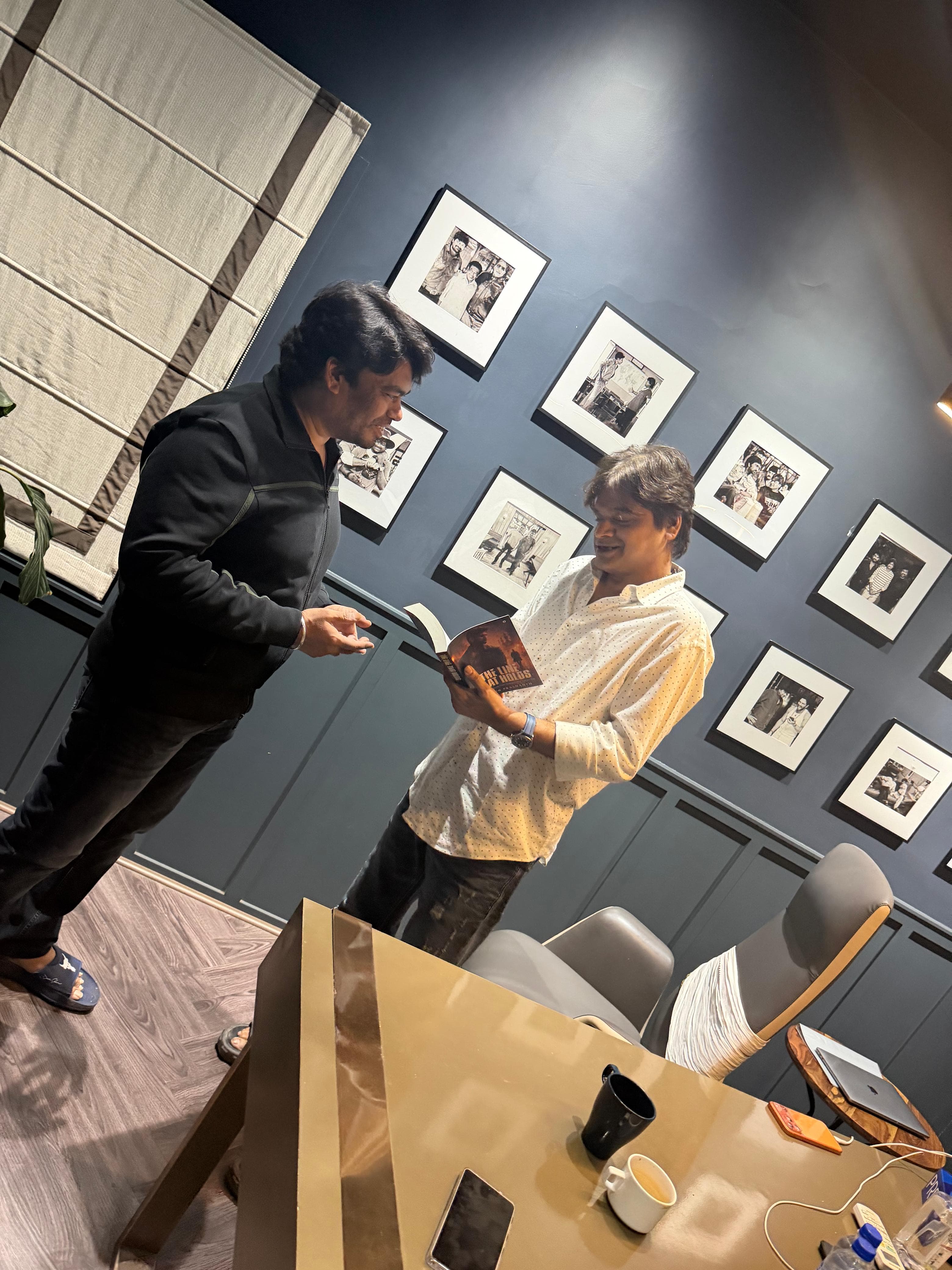 The same photo-lined office, the two men looking over the copy of The Line That Holds from a different angle