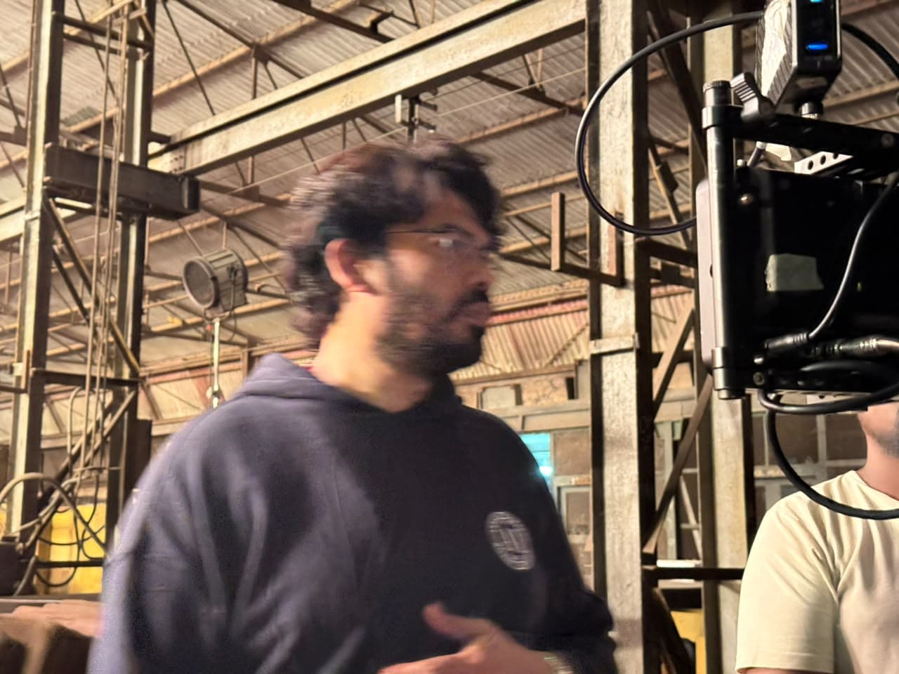 A man in motion beside a camera monitor on a film set, mid-turn with a blurred gesture