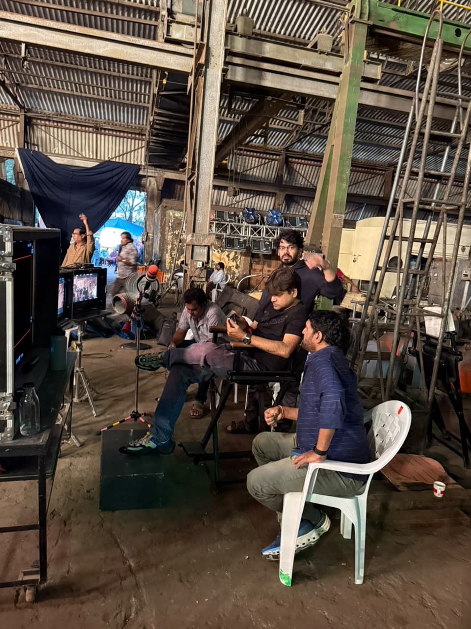 Wide shot of film crew members seated near camera monitors inside a warehouse studio